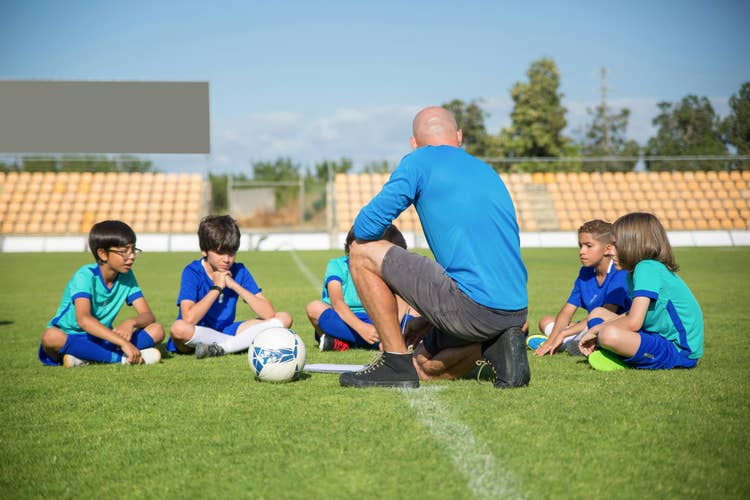 Recreational soccer coach sitting with his team on the field