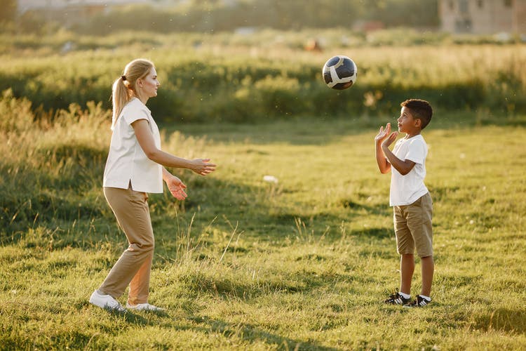 Parent and young child playing soccer together in a golden field