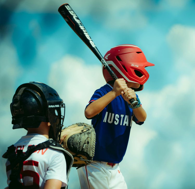 Youth baseball batter at the plate under a bright blue sky
